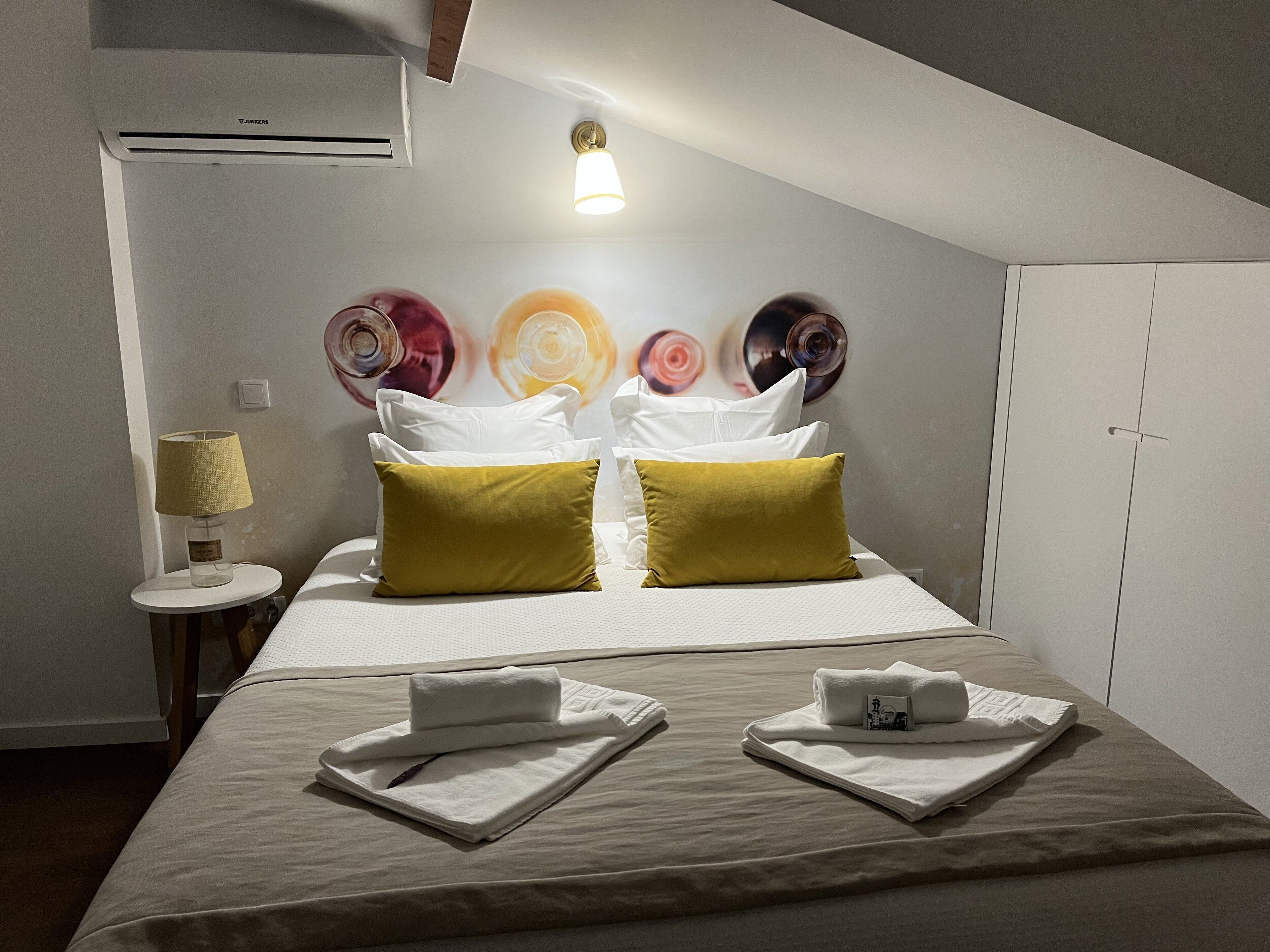 A hotel room with a bed, two pillows, a bedside lamp, a wall art piece, and a wardrobe.