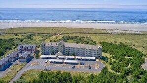 An aerial view of a hotel with a parking lot, a beach in the background, and surrounding greenery. - Amazing Ocean Views, Pets Ok, Walk To Town and Beach (Breeze) (Long Beach)