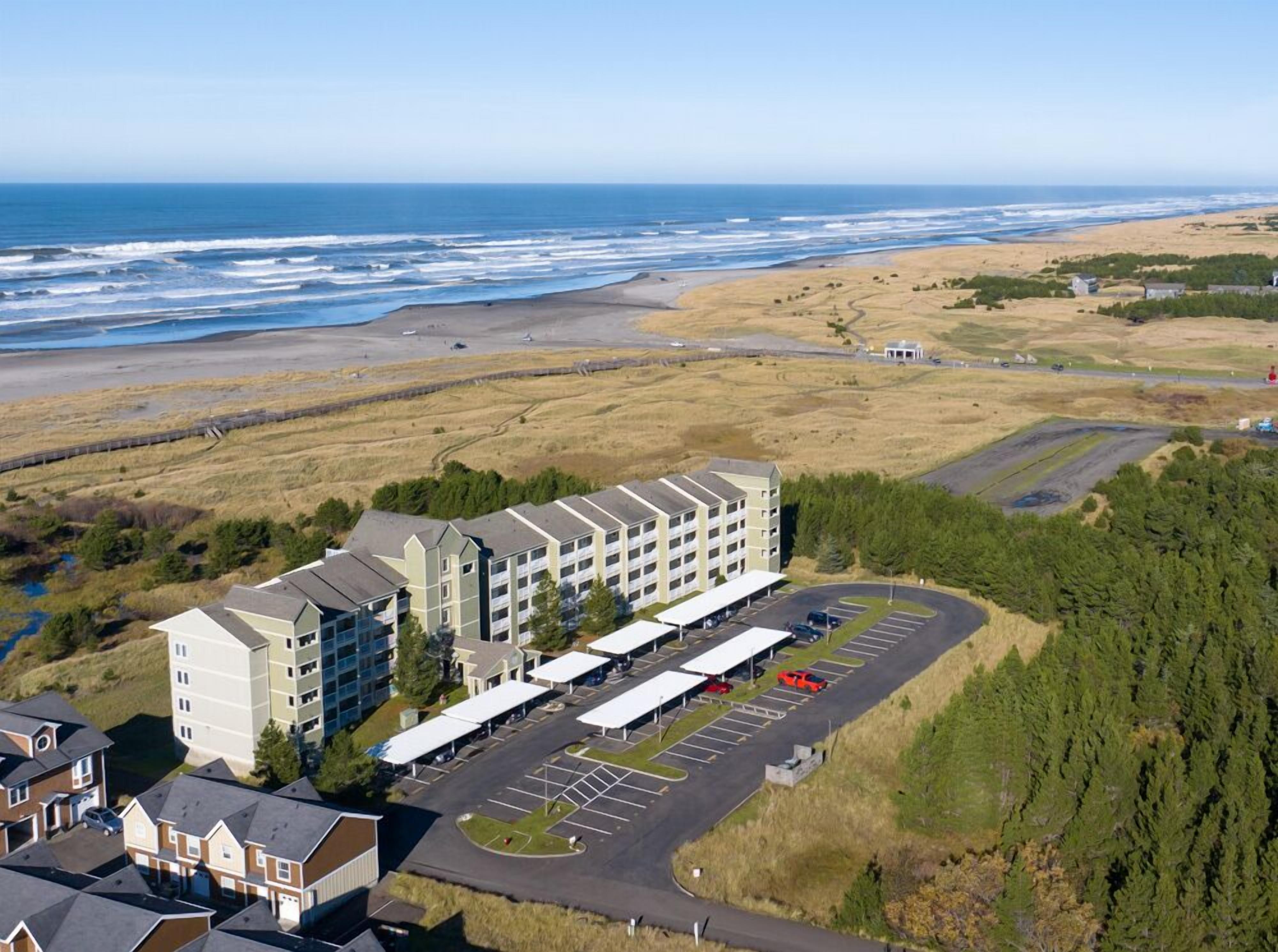 A multi-story hotel with a parking lot and a view of the beach and ocean.