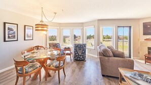 A spacious living area with a dining table, comfortable seating, and large windows offering a view of the outdoors. - Amazing Ocean Views, Pets Ok, Walk To Town and Beach (Breeze) (Long Beach)
