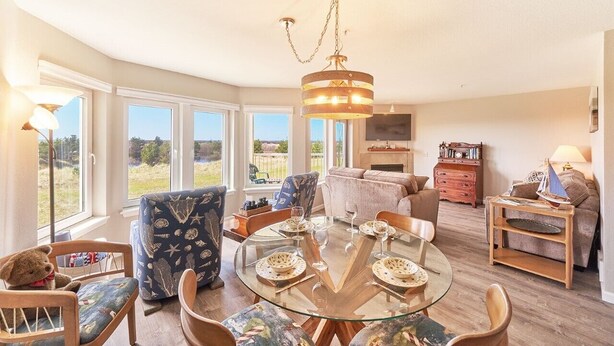 A cozy living room with a glass dining table, comfortable seating, a large window with a view, and a hanging light fixture. - Amazing Ocean Views, Pets Ok, Walk To Town and Beach (Breeze) (Long Beach)