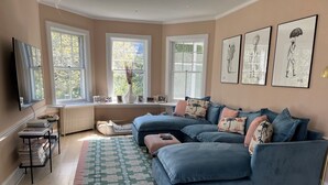 Un salon avec un canapé d’angle bleu, un tapis à motifs et une grande fenêtre donnant sur les arbres.