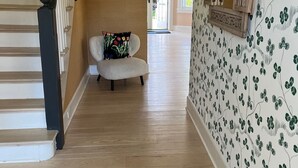 Un couloir avec un escalier, une chaise dotée d’un coussin à motifs floraux et un mur orné d’un papier peint à motifs.
