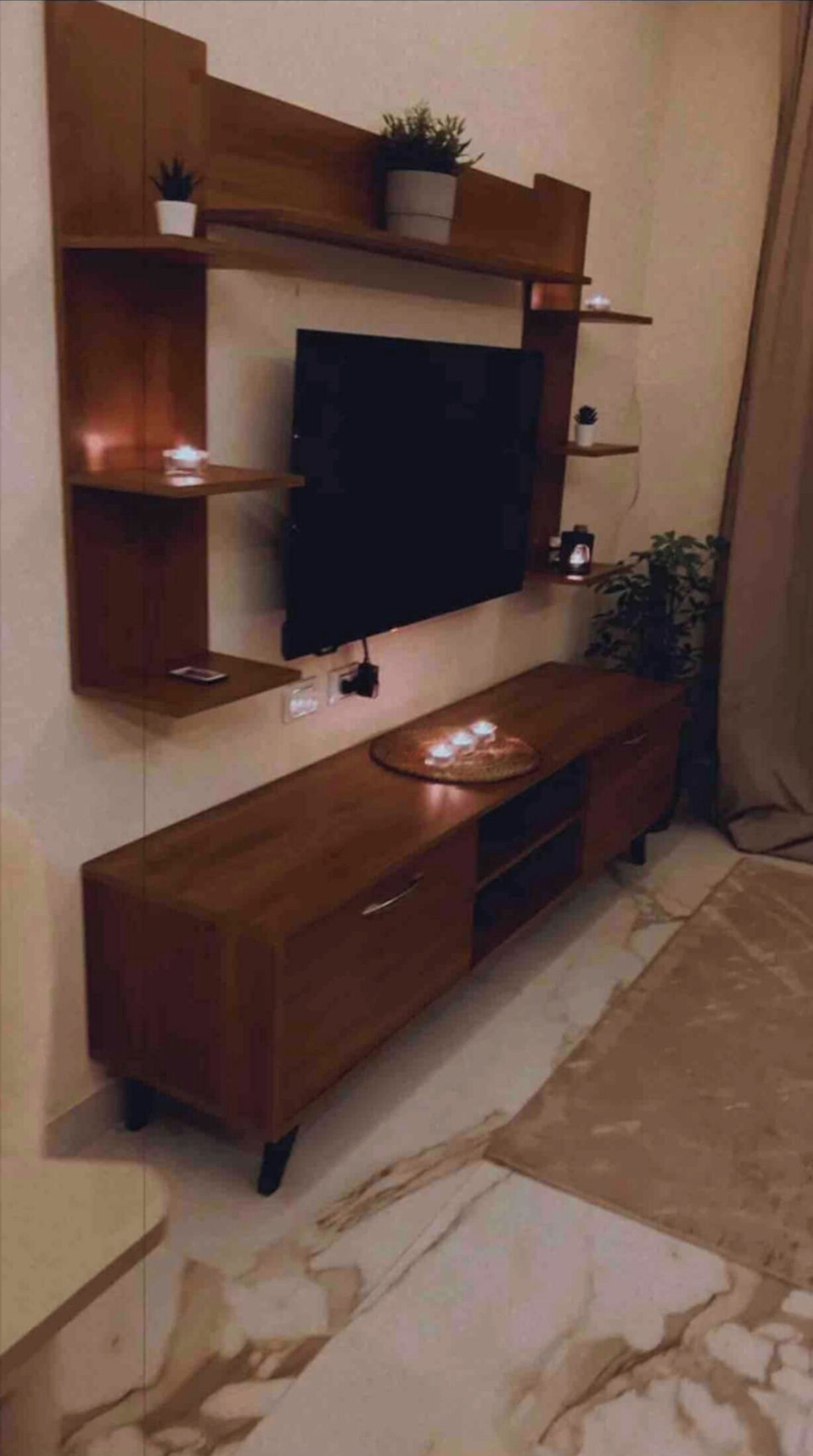 Ein modernes Wohnzimmer mit einem Holz-TV-Möbel, einem flachbildfernseher an der Wand und einem kleinen Topfpflanz auf dem Regal.