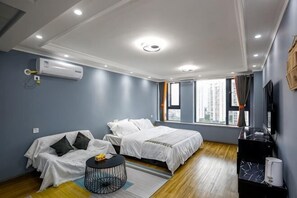 A hotel room with two beds, a sofa, a small round table, a TV, and a window with a view of buildings.