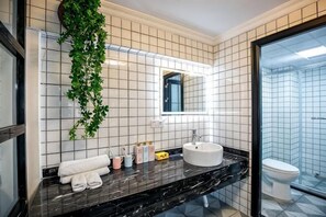 A bathroom with a black marble countertop, white tiles, a white sink, a mirror, a toilet, and a hanging plant. - Huayuan Homestay (Huangshang Scenic Area South Gate) (Huangshan City)