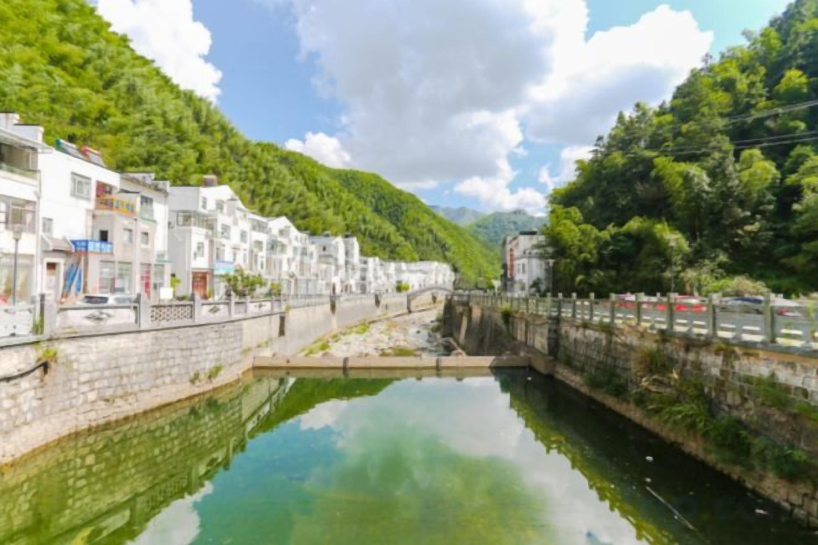 Un canal estrecho bordeado por edificios, un puente de piedra y un promontorio cubierto de bosque.