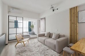 A modern living room with a sofa, a wooden dining table, a chair, and a large window.