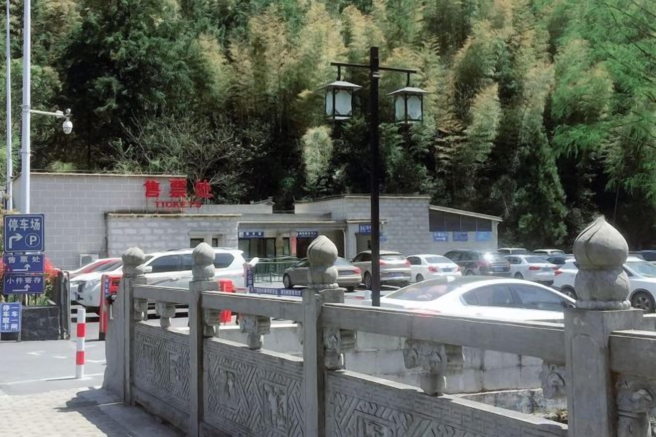 A parking area with cars, a stone wall, and a building with a sign.