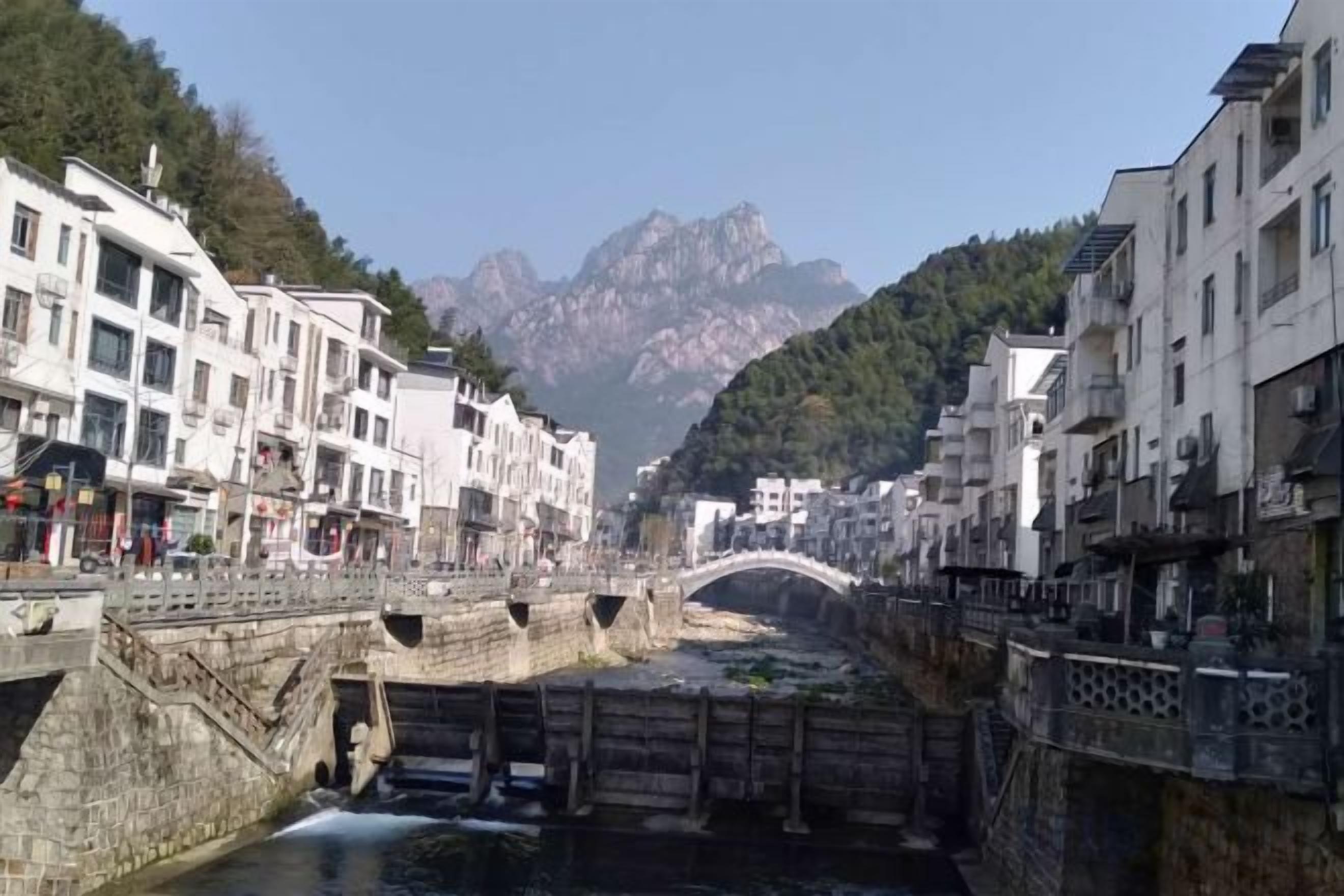 Un pueblo a orillas del río con puentes de piedra, edificios y montañas al fondo.