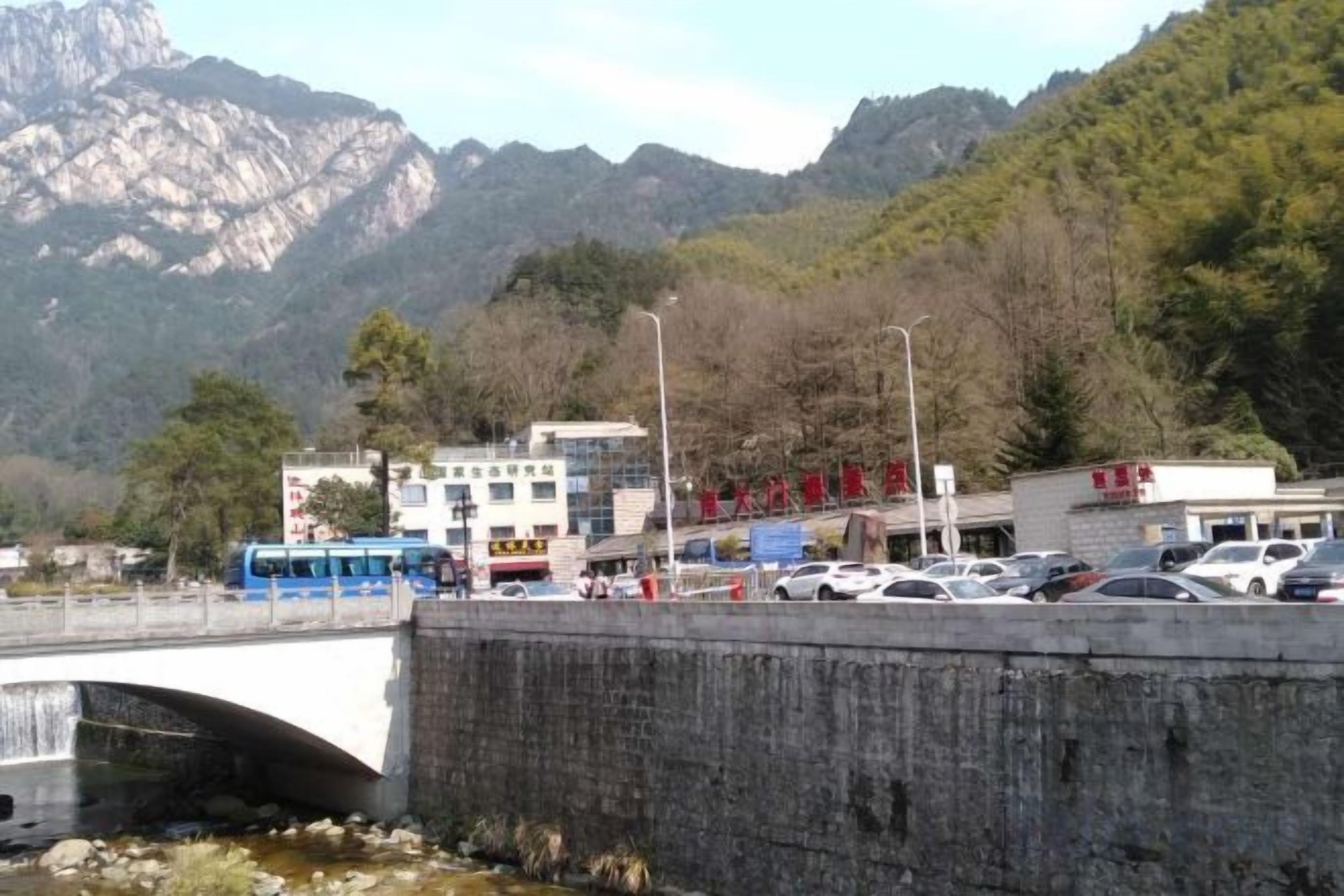 Un puente sobre un río con montañas al fondo, un estacionamiento con automóviles y edificios con señalización.
