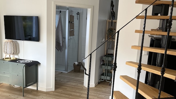 Ein modernes Interieur mit einer Holztreppe, einem Flachbildfernseher und einem Korbstuhl-Beistelltisch.