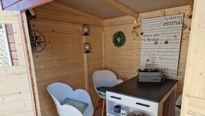 Ein gemütliches Blockhaus-Interieur mit Holzwänden, einem Kompass, zwei weißen Stühlen, einem kleinen Tisch mit einem Korb und einem Regal mit Aufbewahrungsbehältern.