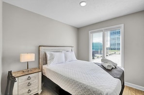 A bedroom with a bed, a nightstand, a lamp, and a window with blinds.