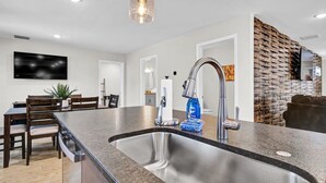 A modern kitchen with a granite countertop, stainless steel sink, and a pendant light.