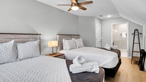 A hotel room with two beds, a ceiling fan, a nightstand with a lamp, and a bathroom door visible in the background.
