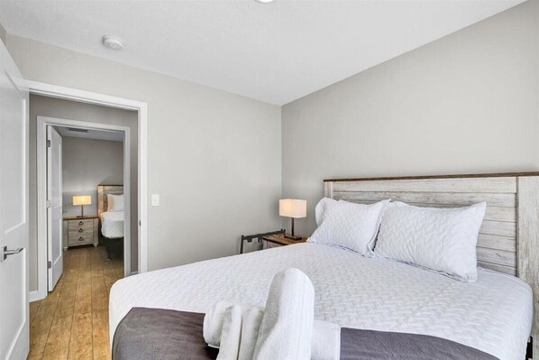 A bedroom with a large bed, a wooden headboard, a nightstand with a lamp, and a door leading to another room.