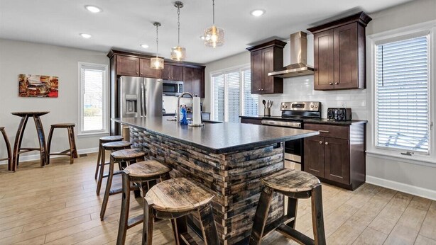 A modern kitchen with a central island, bar stools, stainless steel appliances, and pendant lighting.