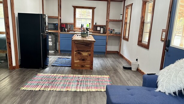 Un'ampia zona giorno con un divano blu, un poggiapiedi marrone e una cucina sullo sfondo.