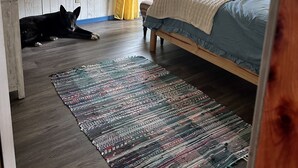 Una camera da letto con un letto, una ventola a soffitto, una finestra con tende e un cane sdraiato sul pavimento.