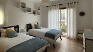 Ein Schlafzimmer mit zwei Betten, einer Deckenleuchte, einem Fenster mit Vorhängen und einer Wanduhr.