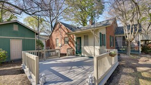 Ett trädäck med räcken, en liten byggnad av tegel med en grön dörr och en vit byggnad med ett fönster.