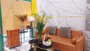 Ein modernes Wohnzimmer mit einem braunen Sofa, einem Glastisch, einem Holznachttisch, einer Vase mit Blumen und einem Obstkorb.