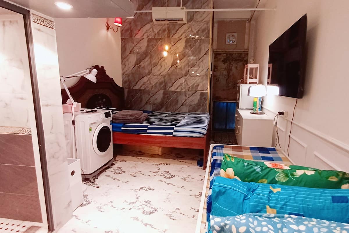 Une chambre d’hôtel de taille réduite, comprenant un lit, un lave-linge, une télévision et une petite table avec une lampe.