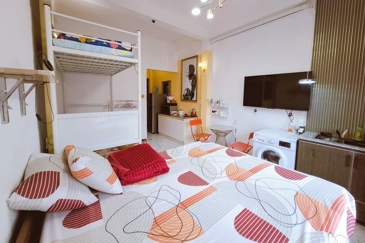 Une chambre avec un lit superposé, un lave-linge, une télévision et un coin cuisine.