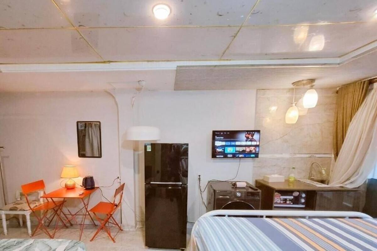 Une chambre d’hôtel compacte comprenant un lit, un bureau avec une chaise, un réfrigérateur, un téléviseur fixé au mur et un petit coin cuisine.