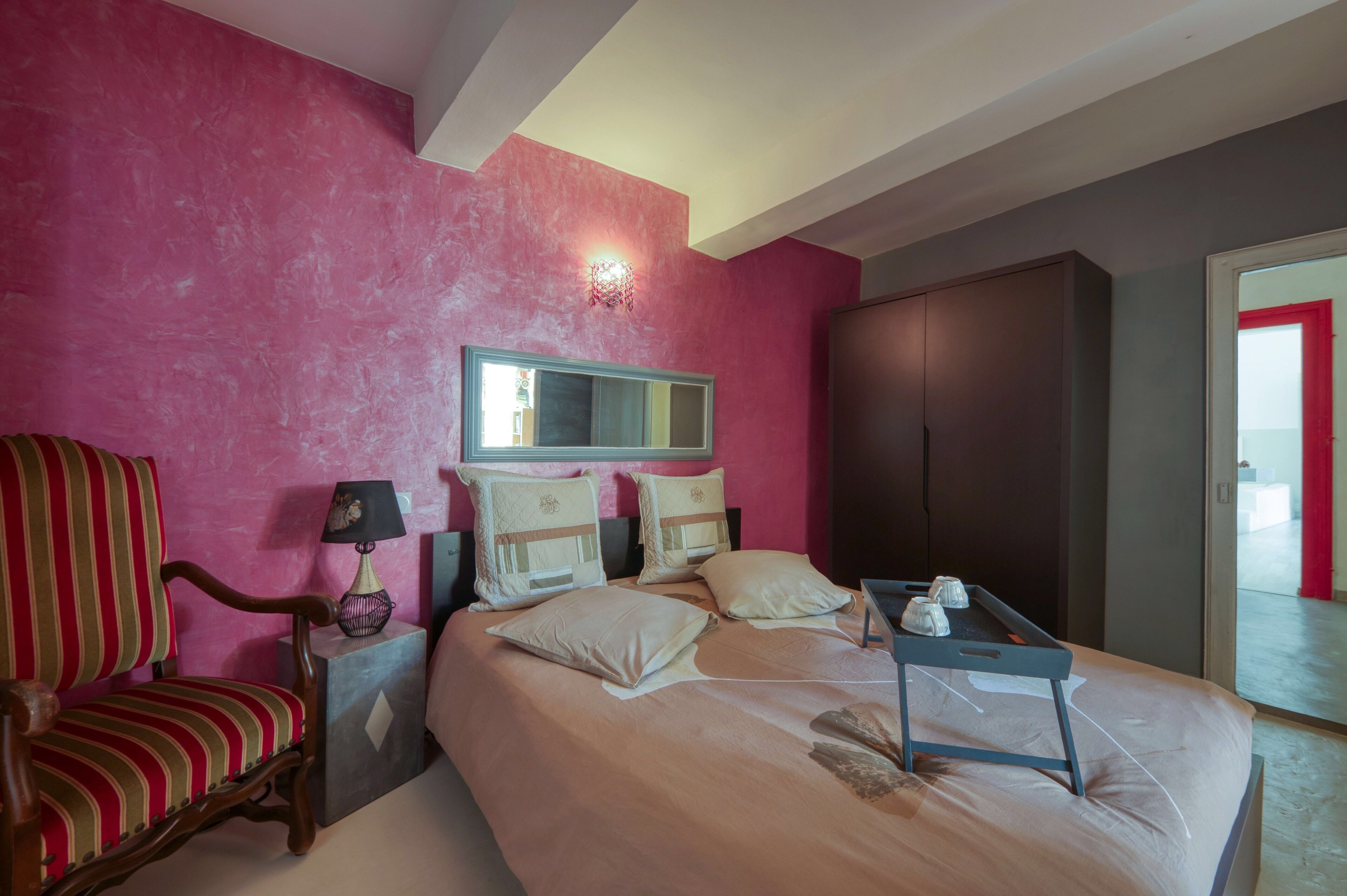 A hotel room with a bed, a chair, a nightstand, a lamp, a dresser, and a mirror.