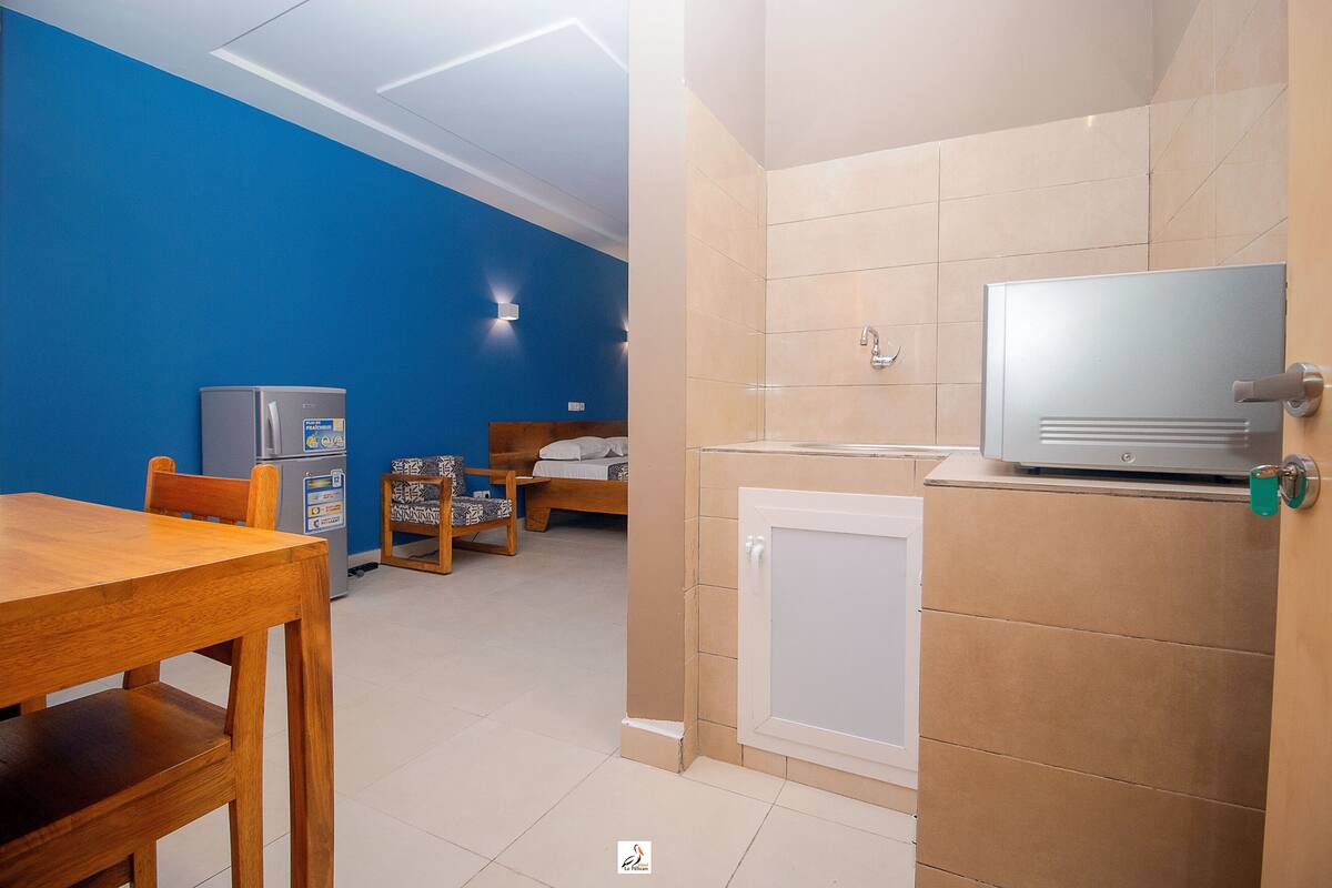 Habitación de hotel compacta con kitchenette, una pequeña mesa de comedor, una cama y un televisor.