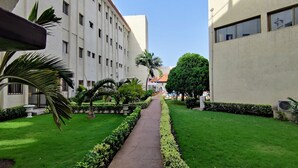 A courtyard with a central pathway flanked by neatly trimmed hedges and palm trees. - Hotel LE PELICAN (Lomé)