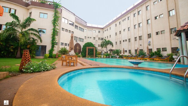 Una piscina con sillas de descanso y una mesa, rodeada por un edificio de varios pisos y balcones.