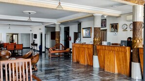 Un vestíbulo con mostradores de recepción de madera, suelo de mármol y una zona de estar con sillas y un banco.