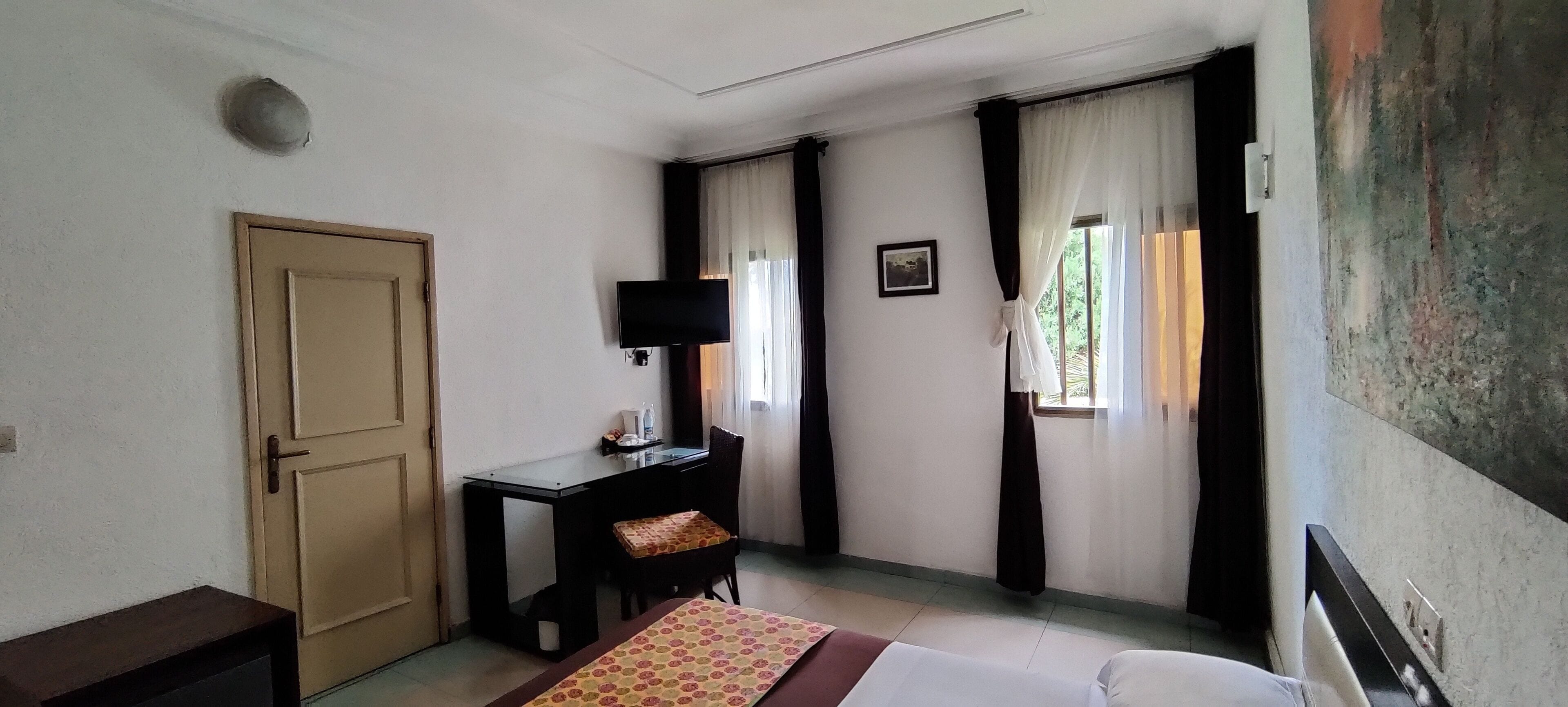 A hotel room with a bed, a desk, a chair, a television, and a door.