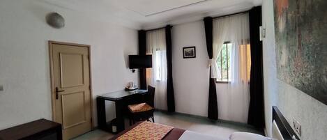 A hotel room with a bed, a desk, a chair, a television, and a door.