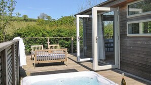 A hot tub on a wooden deck with a sofa and a glass door leading to a room. - 7 Valley View (Looe)