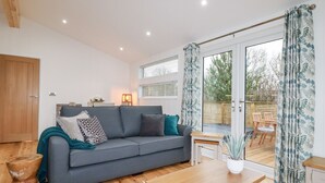 A modern living room with a grey sofa, wooden coffee table, and a view of the outdoor patio. - 7 Valley View (Looe)
