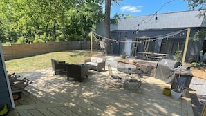 Une terrasse en bois, dotée de mobilier d’extérieur, d’un barbecue et d’une guirlande lumineuse.