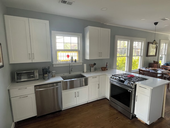 A kitchen with white cabinets, a stainless steel sink, a built-in oven, and a window with a view of greenery.