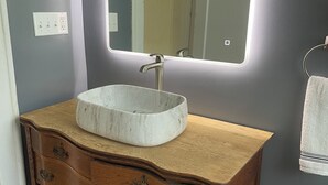 Une salle de bain avec un lavabo en marbre, un meuble-lavabo en bois, un miroir avec éclairage intégré, un porte-serviettes et un porte-rouleau de papier toilette.