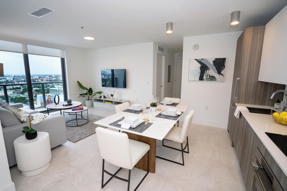 A modern kitchen and dining area with a large window, a flat-screen TV, and a dining table set for four.