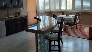 A kitchen with dark cabinets, a sink, and a window with blinds. There is a dining area with a round table, chairs, and a rug. - Romantic Villa Beach House (San Carlos)