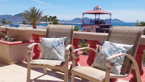 Two cushioned chairs with patterned cushions on a tiled terrace overlooking a scenic view of the sea and mountains. - Romantic Villa Beach House (San Carlos)