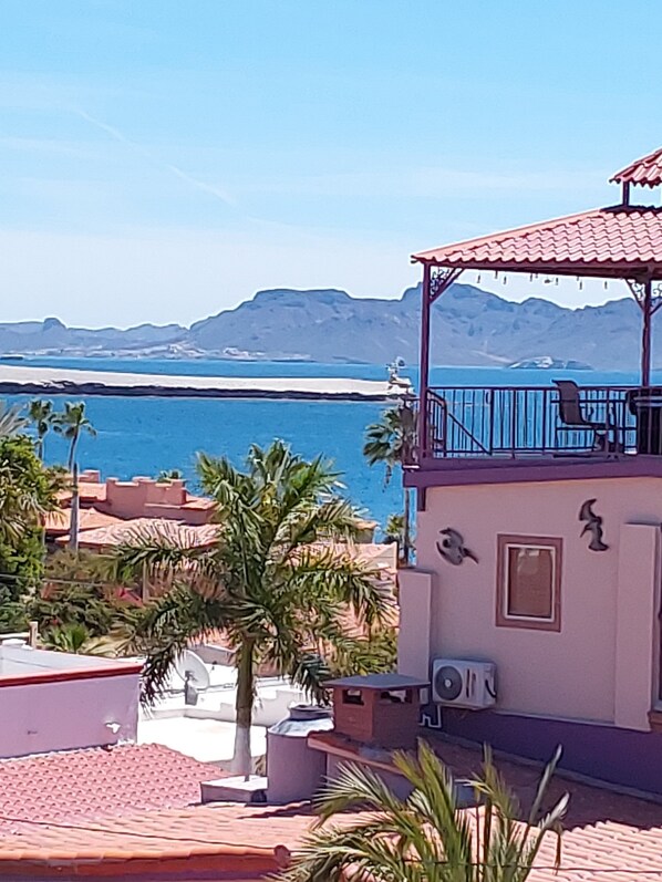 A building with a red-tiled roof, a balcony, and a view of the sea and mountains.