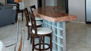 A dining area with a marble floor, a round table with chairs, a painting on the wall, and a kitchen area with a refrigerator. - Romantic Villa Beach House (San Carlos)