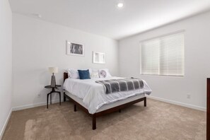 Cozy retreat with a single bed, round table, and framed picture, set against a serene backdrop.