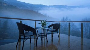 Een balkon met een tafel en stoelen, met uitzicht op een bergachtig landschap gehuld in mist.