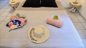 Un lit bien fait, avec deux oreillers noirs, une paire de serviettes enroulées, un chapeau de paille et un éventail.